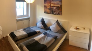 A bedroom with a bed, a nightstand, a window, and a painting on the wall. - Suite Auenviertel (Erfurt)