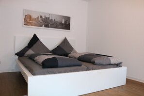 Ein modernes Bett mit weißem Gestell und grauer Bettwäsche, ein Stadtlandschaftsposter an der Wand und ein Holzboden.