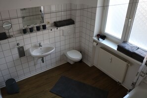 Ein Badezimmer mit Waschbecken, Toilette und Spiegel. Ein Fenster mit Handtuch auf der Fensterbank.