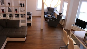 A modern living room with a sofa, a dining table with chairs, a TV, and a bookshelf. - Suite Auenviertel (Erfurt)