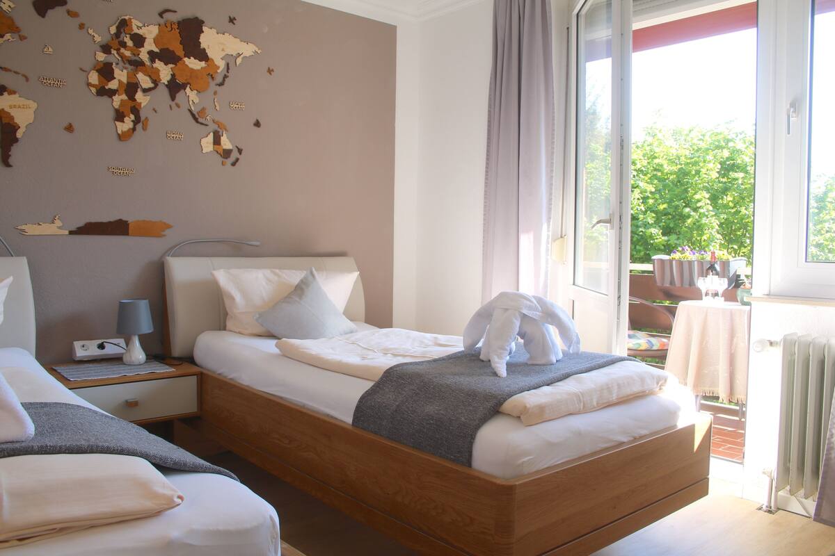 A bedroom with a wooden bed, a nightstand, a world map on the wall, and a view of the outdoors.