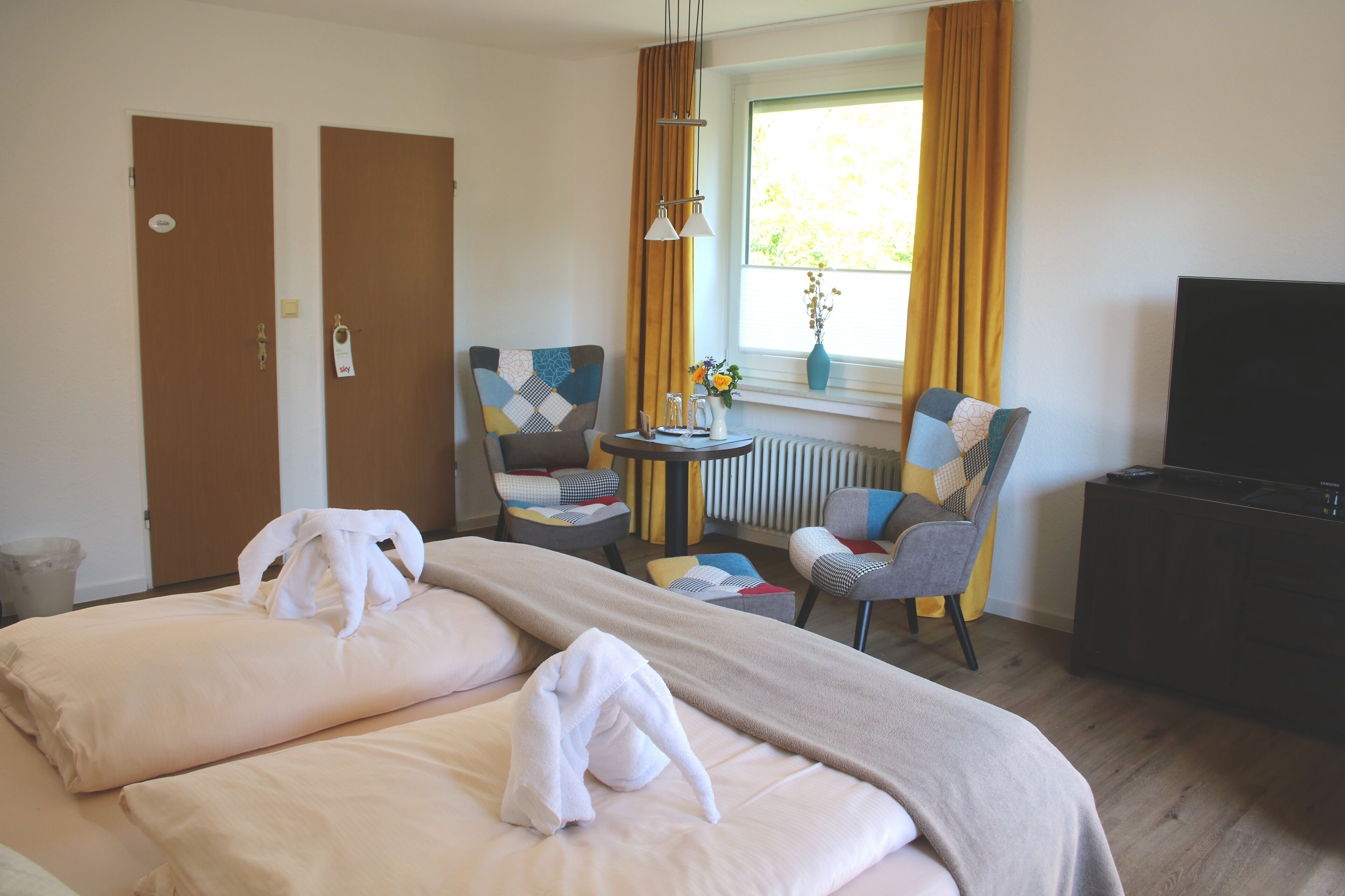 Een hotelkamer met twee bedden, een televisie, een klein tafeltje met een vaas en twee stoelen.