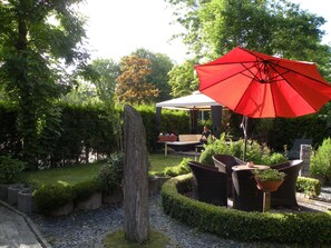 Um jardim com um guarda-sol vermelho, área de estar ao ar livre e um viveiro bem cuidado.