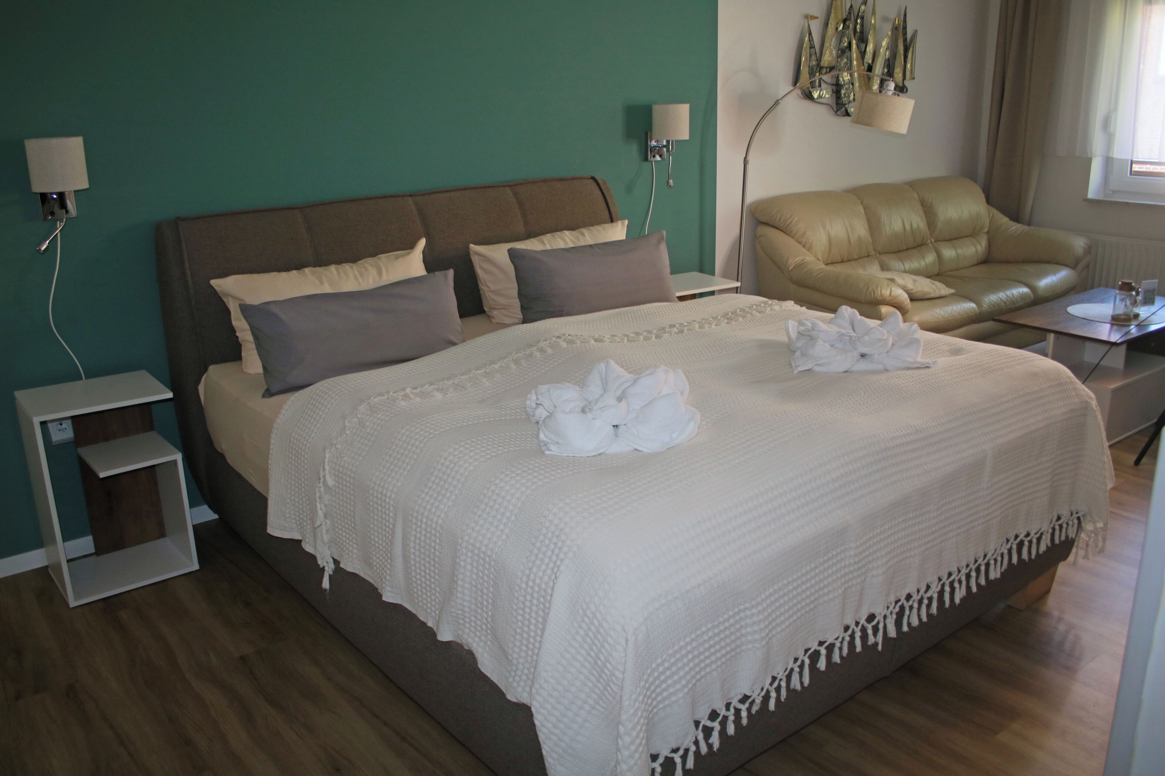 Una cama bien hecha con edredón blanco y almohadas, un sofá de cuero y una mesita de noche con lámpara.