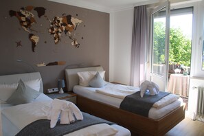 Quarto de hotel com duas camas, um mapa-múndi na parede, uma janela com vista para áreas verdes e uma mesa com abajur.