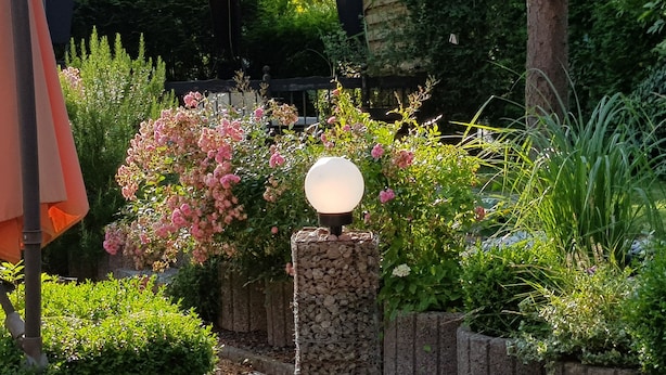 A garden with a gazebo, a stone pillar with a spherical light, and various plants. - Hotel Garni Kröger (Wittmund)