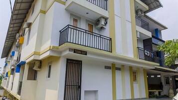 Um edifício residencial de vários andares, com varandas, entrada fechada por portão e área de estacionamento coberta.