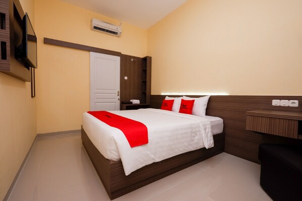 A hotel room with a bed, a desk, a chair, an air conditioning unit, and a television. - RedDoorz Plus near Paragon Mall Semarang (Semarang)