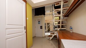 A room with a white door, a yellow wall, a staircase, and a kitchen area with a countertop and sink. - RedDoorz Plus near Paragon Mall Semarang (Semarang)