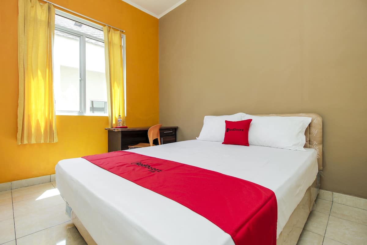 A hotel room with a bed, a desk, and a window with curtains.