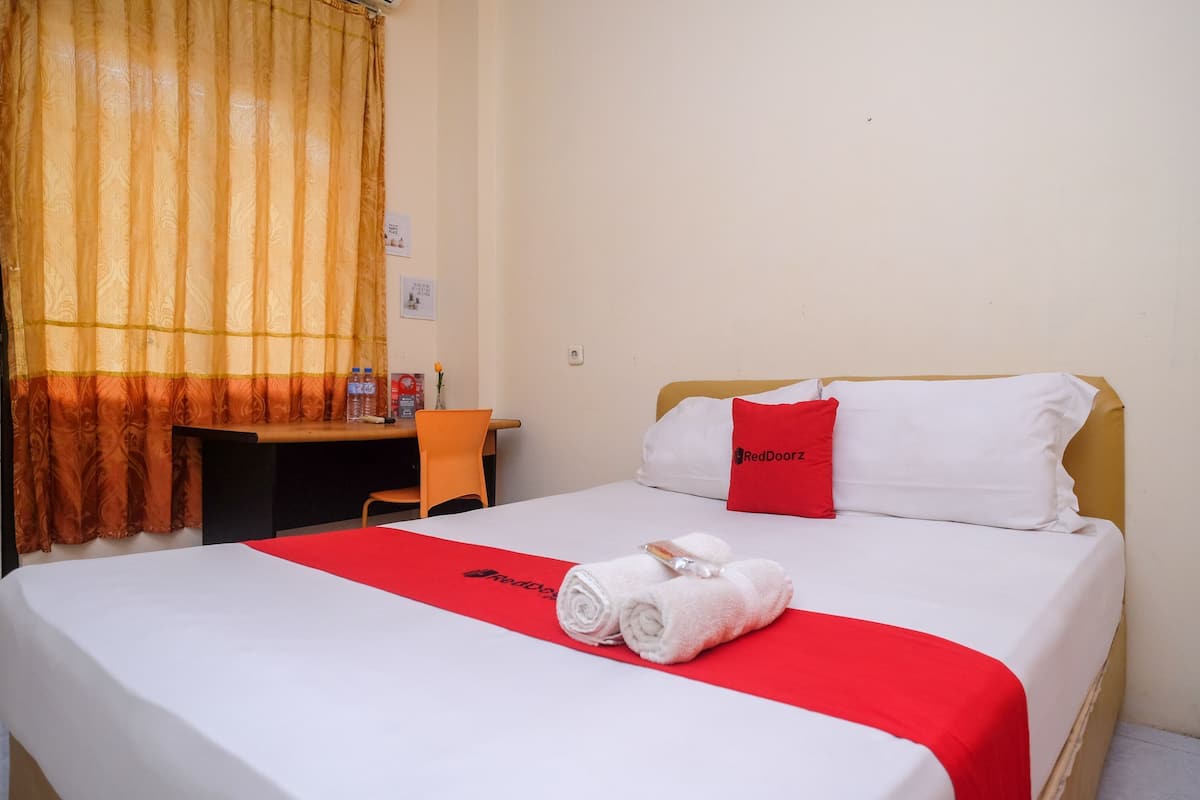 A hotel room with a bed, a desk, and a chair. There are towels on the bed and a Red Door sign on the pillow.