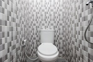 A bathroom with a tiled floor, a toilet, and a shower area. - RedDoorz near Sam Ratulangi Airport (Manado)