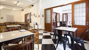 Un comedor con sillas y mesas de madera, suelo a cuadros y vista a través de una puerta con marco de madera.