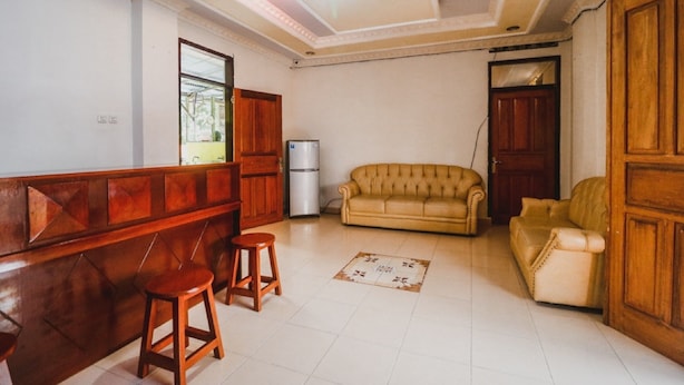 Una sala de estar con un banco de madera, dos taburetes, un sofá color beige y un refrigerador.