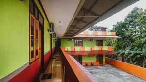 Un pasillo con barandilla roja, paredes verdes y un pequeño patio con un edificio de techo rojo.