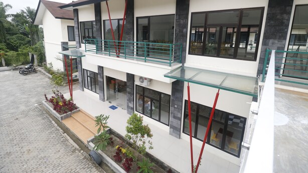 Ein modernes, zweistöckiges Gebäude mit Balkon, großen Fenstern und einer gepflasterten Auffahrt.