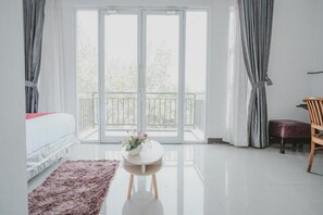 A modern bedroom with a large sliding glass door leading to a balcony, a white bed, a round table with a vase, and a wooden chair. - RedDoorz near Lampung Walk (Bandar Lampung)