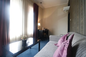A hotel room with a sofa, a small table with a vase of flowers, a desk with a lamp, and an air conditioning unit on the wall. - RedDoorz Plus @ Jalan Raden Intan Lampung (Bandar Lampung)