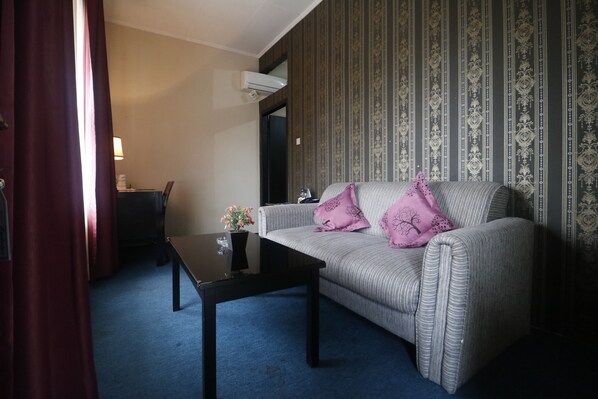 A room with a striped sofa, a small table with a vase, and a patterned wallpaper.