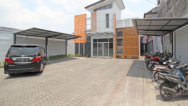 Een modern gebouw met een overdekte parkeerplaats, een auto en meerdere motorfietsen ervoor geparkeerd.
