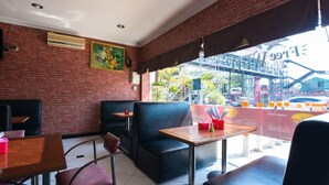 An indoor restaurant with brick walls, black leather booths, and a view of a bridge and palm trees outside. - RedDoorz @ Urip Sumoharjo (Surabaya)