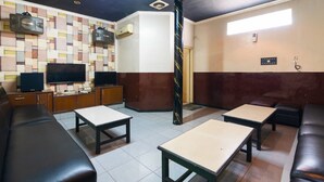 A hotel lobby with a tiled floor, leather sofas, wooden tables, a television, and a patterned wall. - RedDoorz @ Urip Sumoharjo (Surabaya)