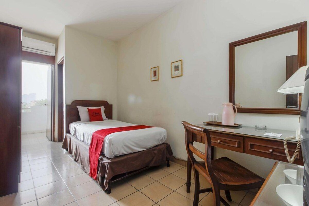 A hotel room with a bed, a desk, a chair, a telephone, and a mirror.