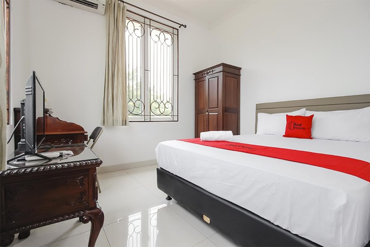 Une chambre d’hôtel comprenant un lit, un bureau avec un ordinateur, une armoire et une fenêtre avec des rideaux.