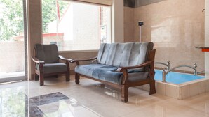 A room with a wooden sofa, a wooden armchair, a glass coffee table, and a small pool. - RedDoorz @ Sedati (Sidoarjo)