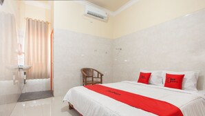 A hotel room with a bed, a chair, a sink, and a shower. - RedDoorz @ Sedati (Sidoarjo)