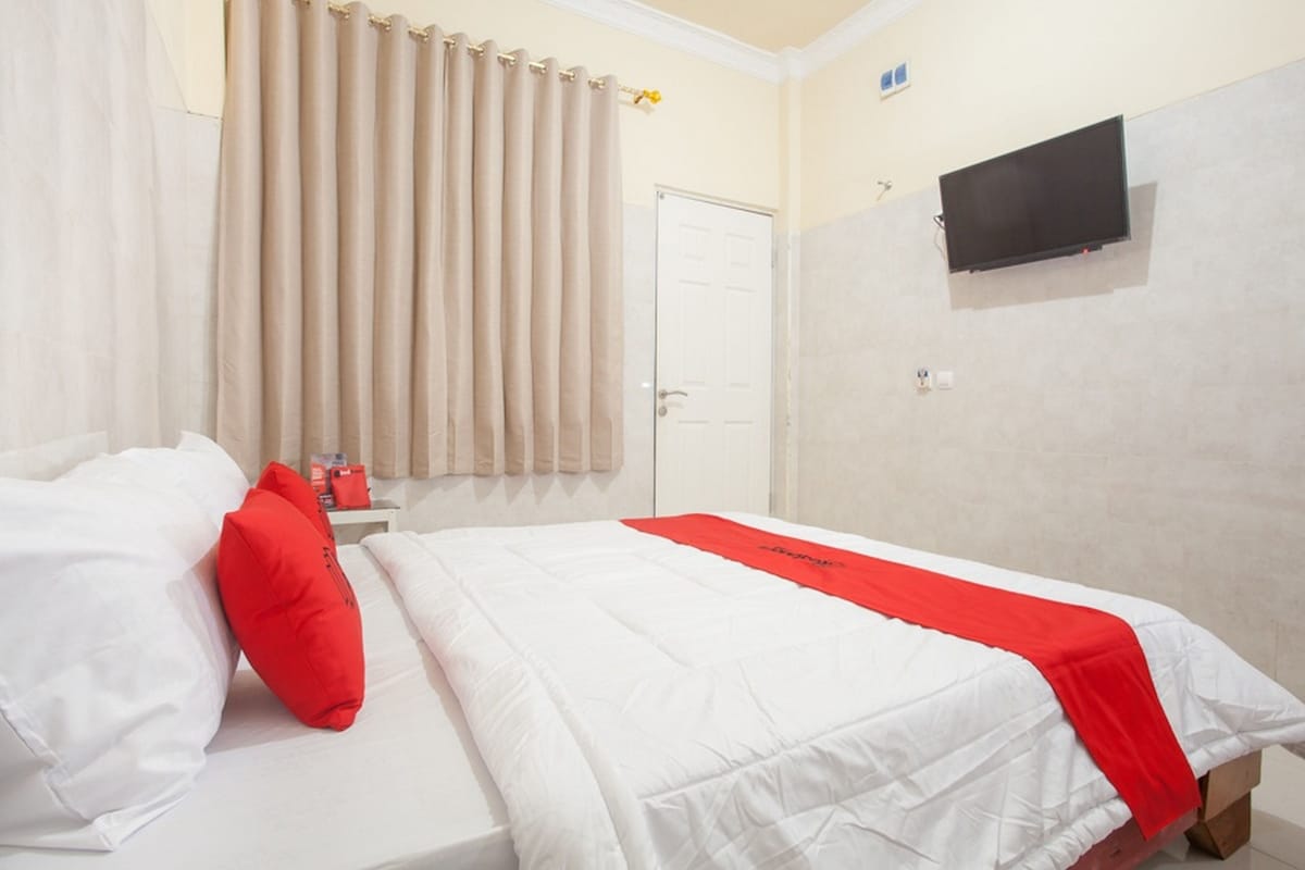 A hotel room with a bed, a TV mounted on the wall, and a window with curtains.