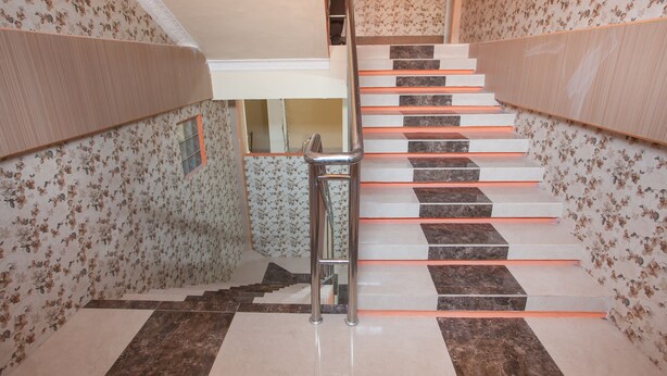 A staircase with alternating dark and light tiles, a metal handrail, and floral wallpaper on the walls. - RedDoorz @ Sedati (Sidoarjo)