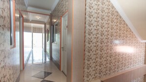 A hallway with patterned wallpaper, a tiled floor, and a wooden staircase. - RedDoorz @ Sedati (Sidoarjo)