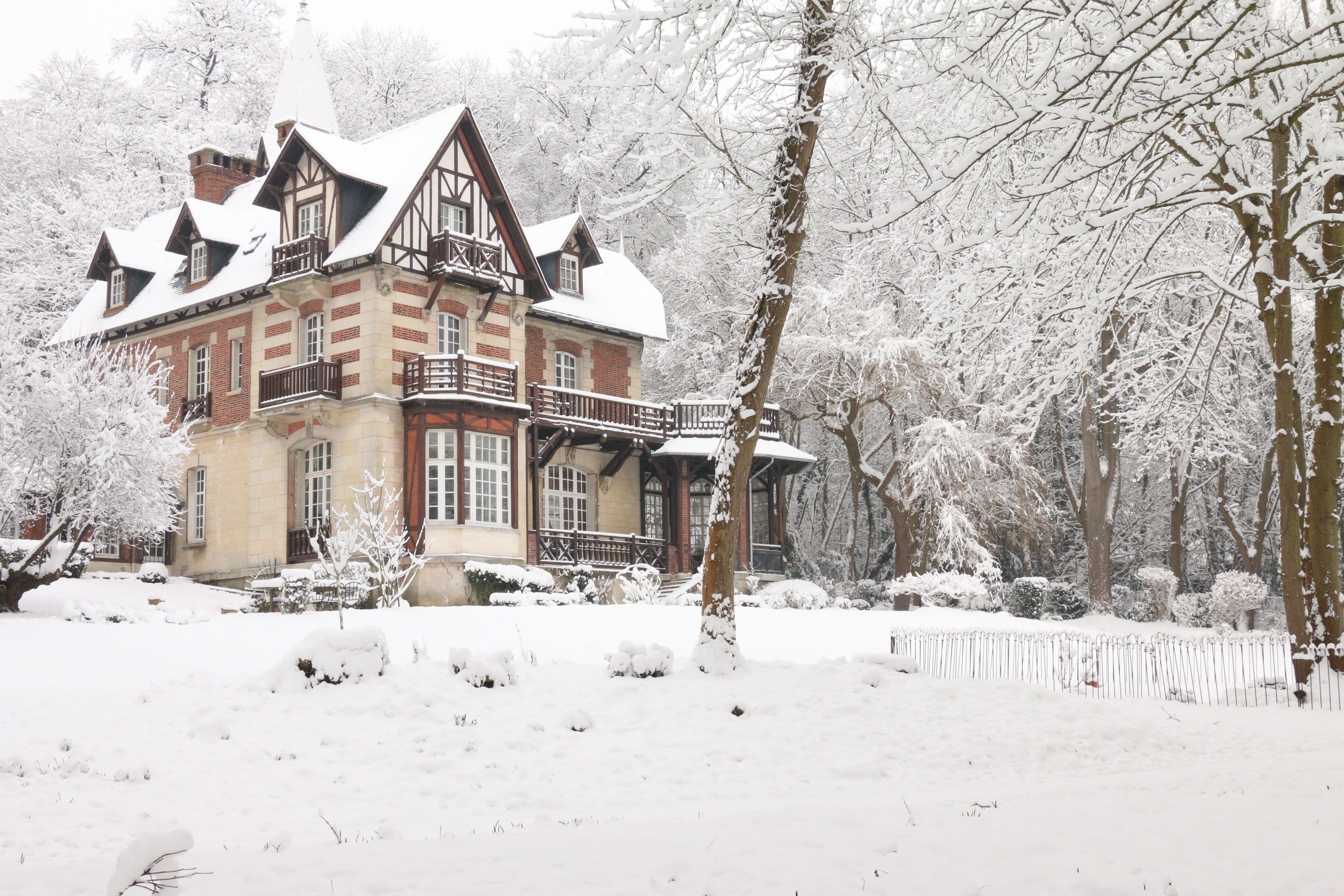 A large, historic building with multiple stories and a prominent balcony, surrounded by snow-covered trees and a fence.