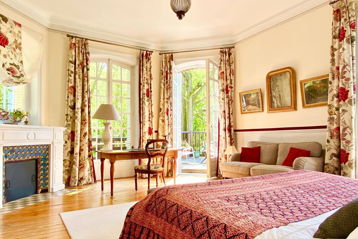 Un dormitorio con una cama grande, un escritorio con lámpara, un sofá y una chimenea.