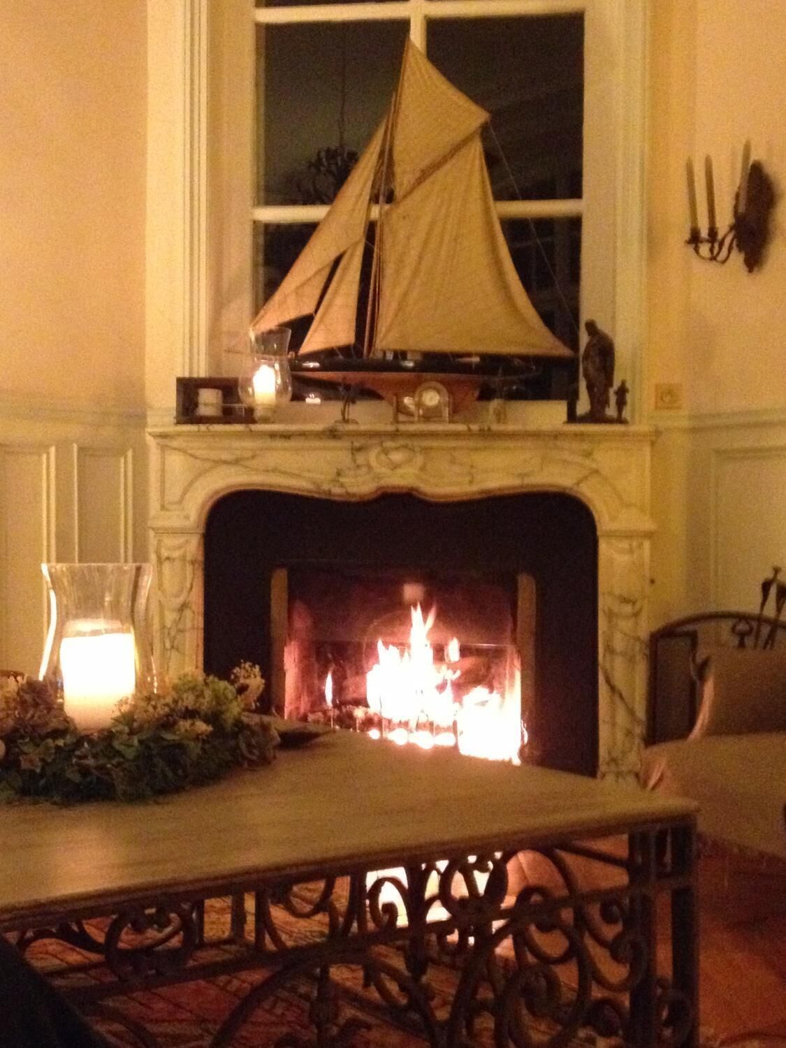 A room with a fireplace, a table with a candle, and a ship model on the mantel.