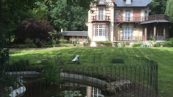 Una casa grande de dos pisos con un césped cuidado y un estanque.
