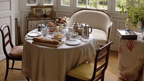 Comedor con una mesa dispuesta para el desayuno, ventanas amplias y vistas a zonas verdes al exterior.