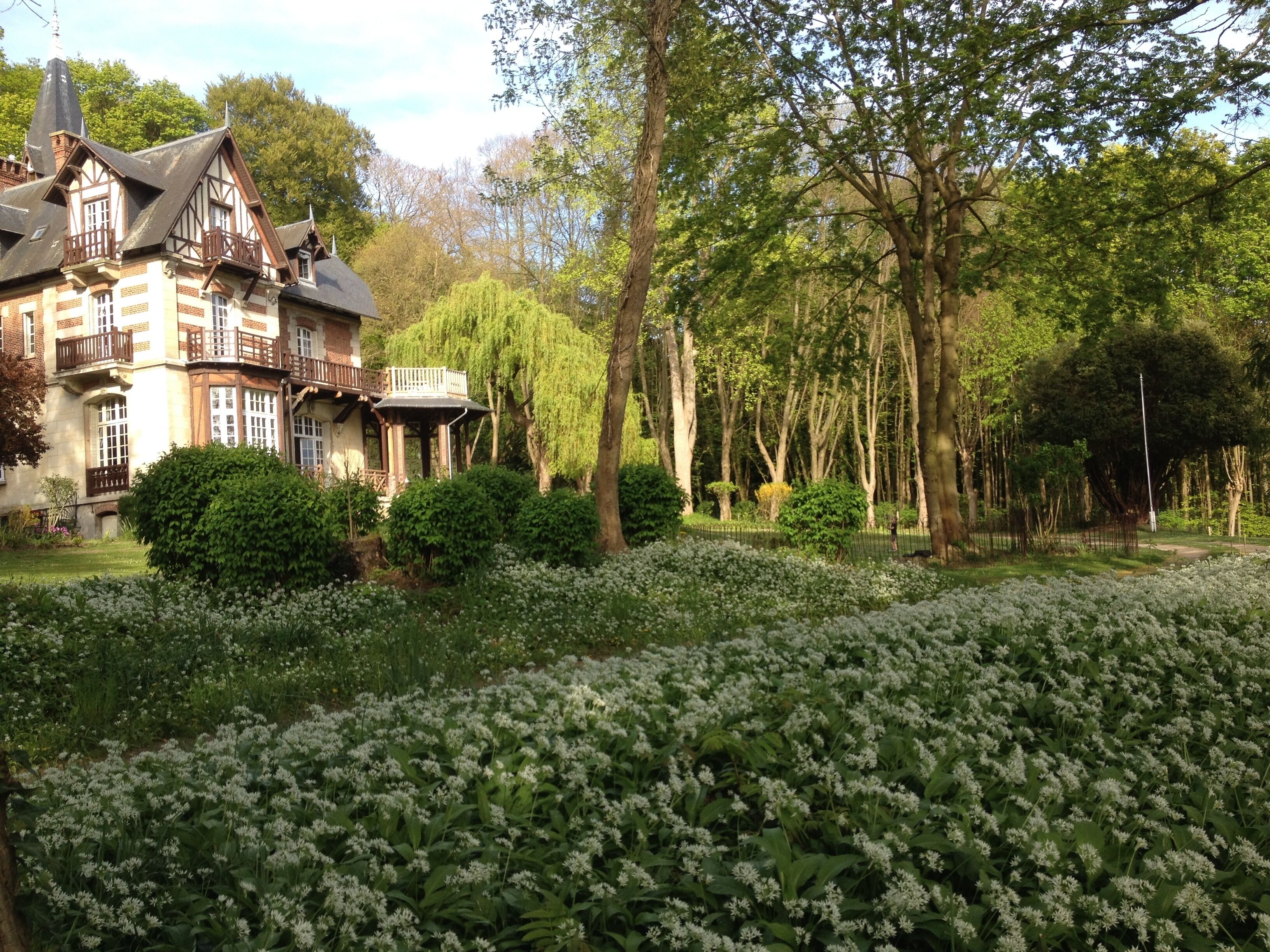 A large, historic building with multiple balconies and a garden with white flowers.
