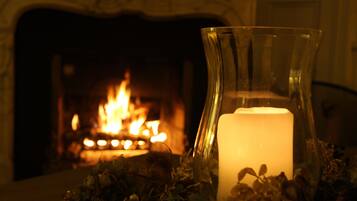 A candle in a glass holder with a fireplace in the background.