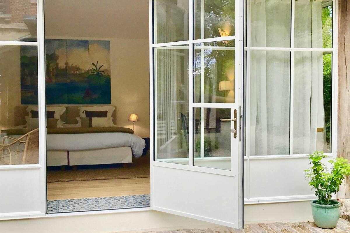 Una habitación de hotel con una cama, un cuadro en la pared y una planta en maceta junto a la ventana.