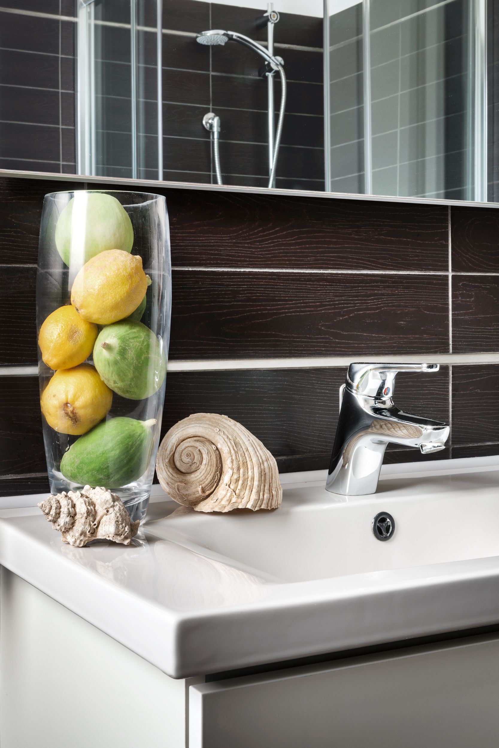 A bathroom with a modern sink, a glass vase with lemons and figs, and a decorative seashell.