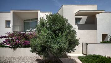 A modern building with a flat roof, a balcony, and a small tree in the foreground.