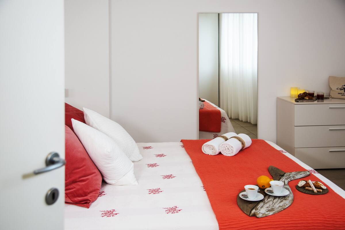 Une chambre d’hôtel avec un lit, une petite table sur laquelle sont disposés des articles pour le petit-déjeuner, et un miroir qui reflète une fenêtre avec des rideaux.