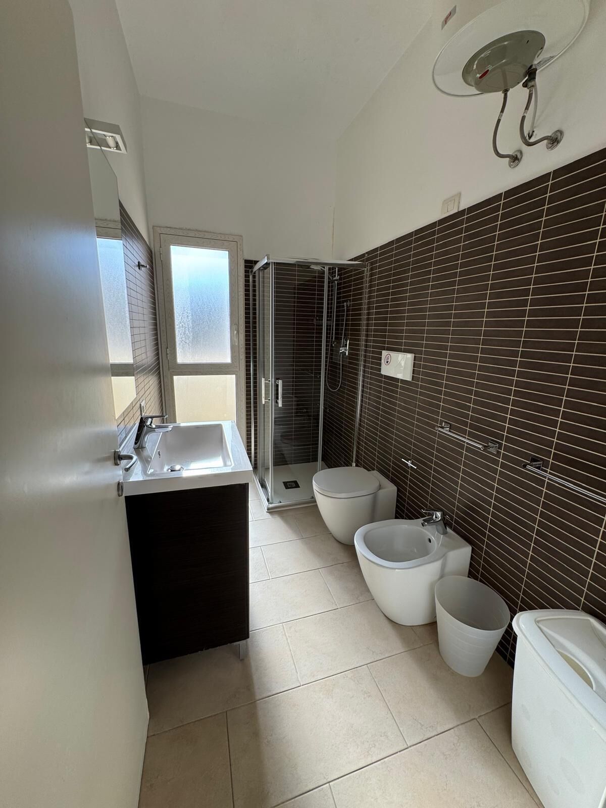 Ein Badezimmer mit Dusche, zwei Bidets, einem Waschbecken und einer Toilette.