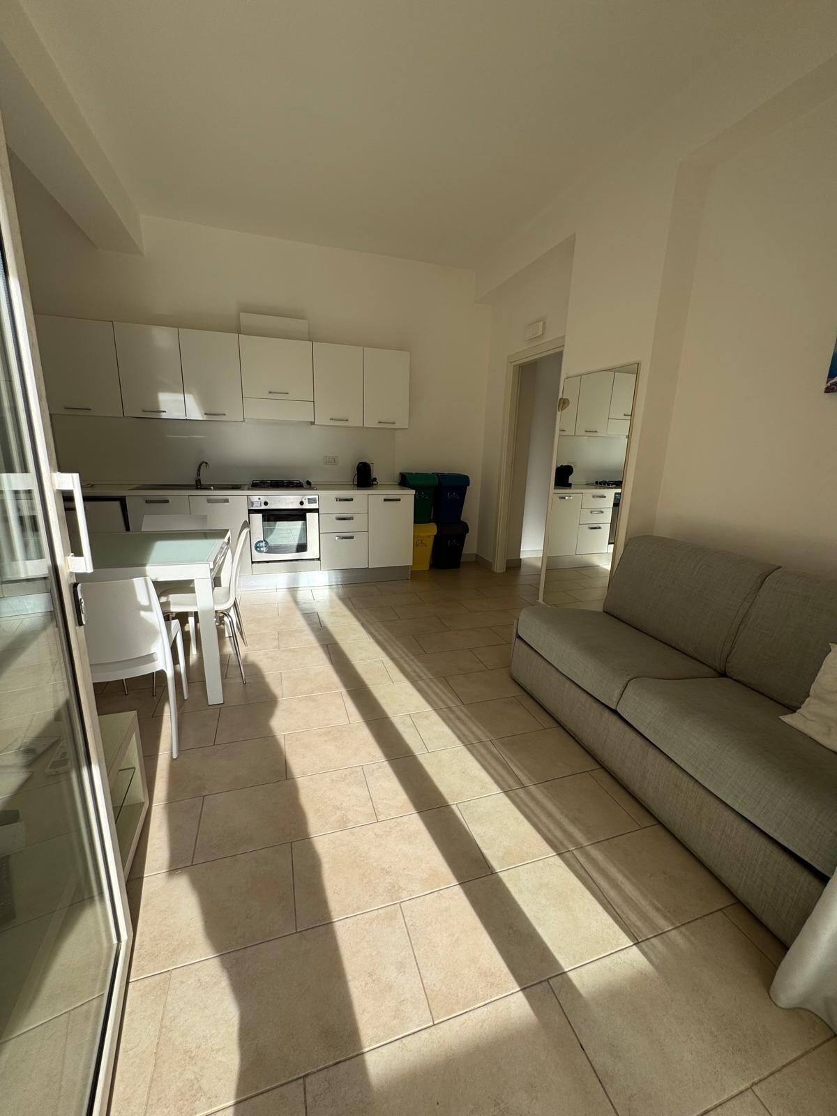 A modern kitchen with white cabinets, a dining area with a table and chairs, and a living area with a sofa.