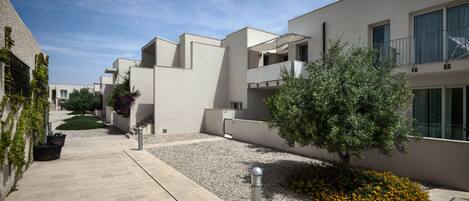 A modern residential building with a clean, geometric design, featuring balconies and a well-maintained garden area.