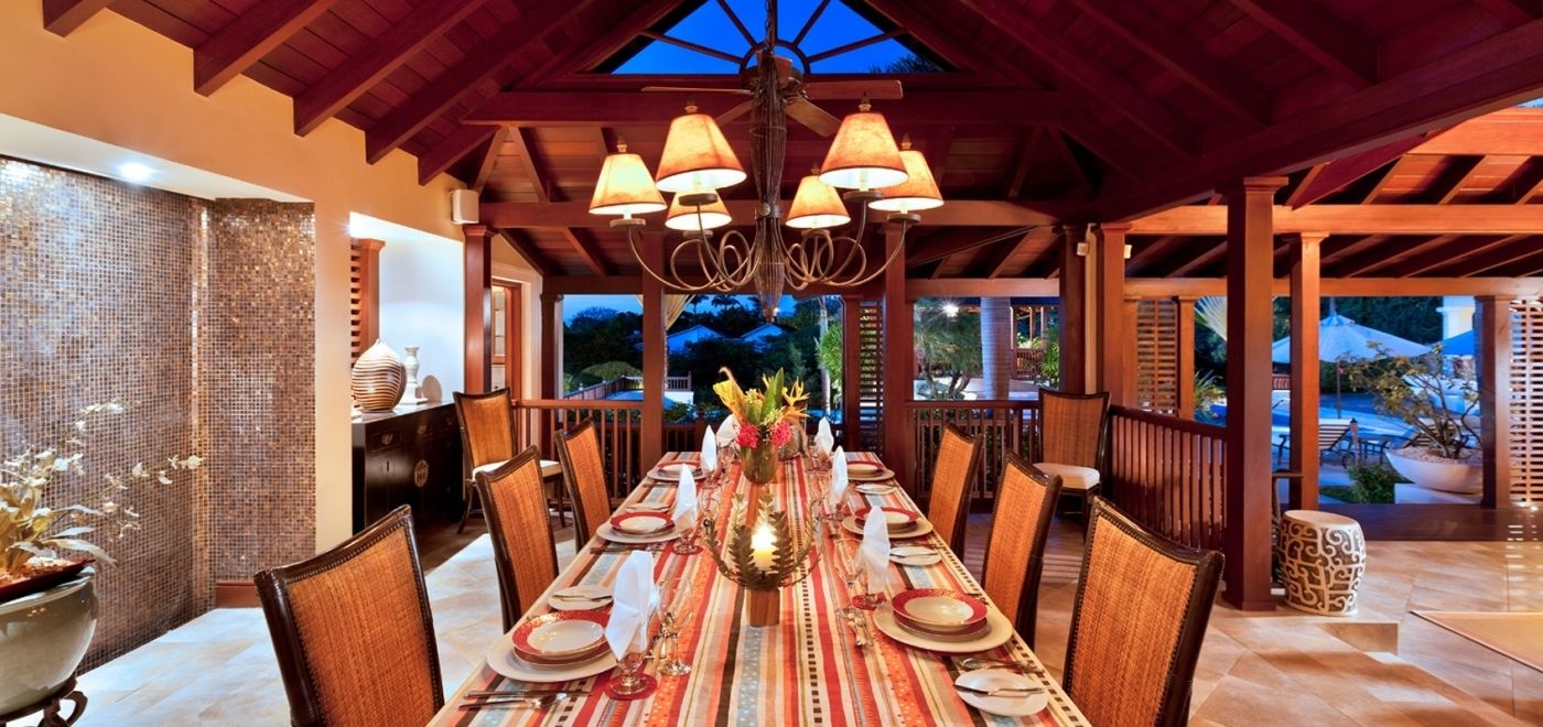 Un comedor con una larga mesa dispuesta para una comida, techo de madera y vistas al exterior.