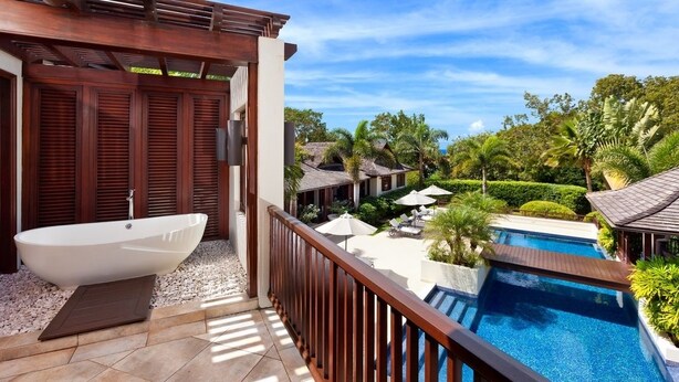 Un balcone con idromassaggio, piscina e vista su una zona resort tropicale.