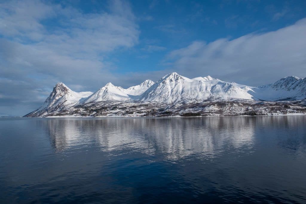 Een bergketen met met sneeuw bedekte toppen die weerspiegeld worden in kalm water.